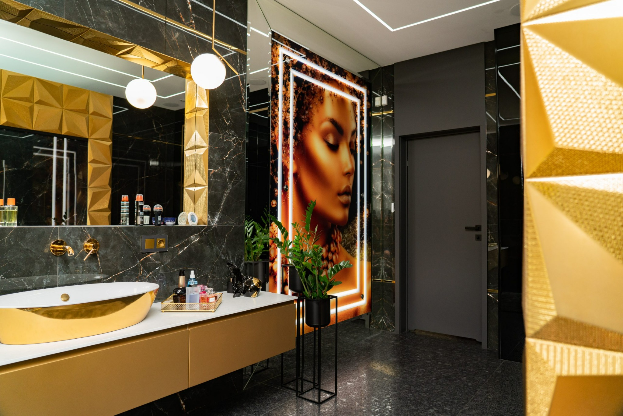 Luksusowa łazienka w czerni i złocie z wolnostojącą wanną, marmurowymi ścianami, podświetlanym portretem kobiety i geometrycznymi elementami dekoracyjnymi.