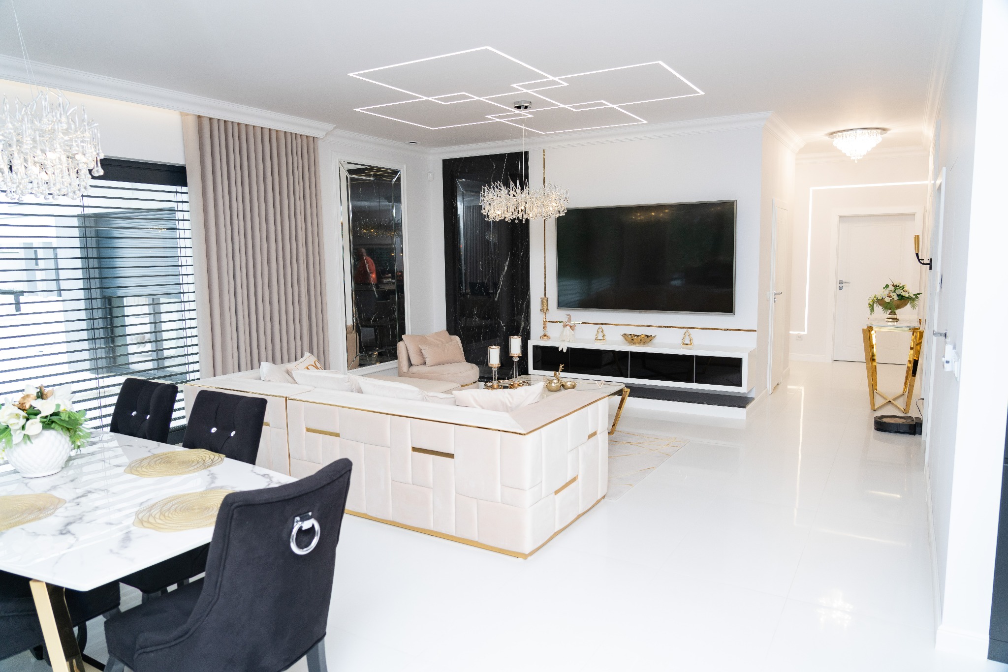 Luksusowy salon z białymi podłogami, beżową sofą z złotymi akcentami, marmurowym stołem jadalnym i nowoczesnym oświetleniem sufitowym.