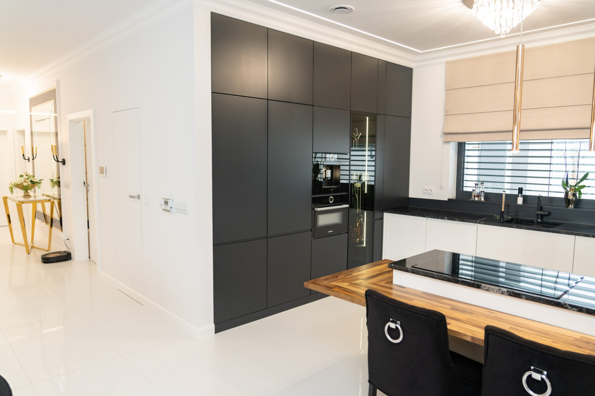 Nowoczesna kuchnia z czarnymi szafkami zabudowanymi do sufitu, drewnianym blatem wyspy i białymi frontami szafek dolnych, uzupełniona o eleganckie oświetlenie i dekoracje.