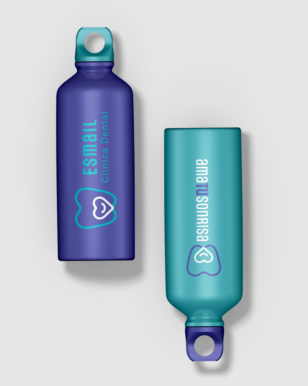 Dwie butelki na wodę z logo firm dentystycznych: fioletowa z napisem 'Esmail Clínica Dental' i turkusowa z 'amatu sonrisa', obie z symbolem zęba w sercu.