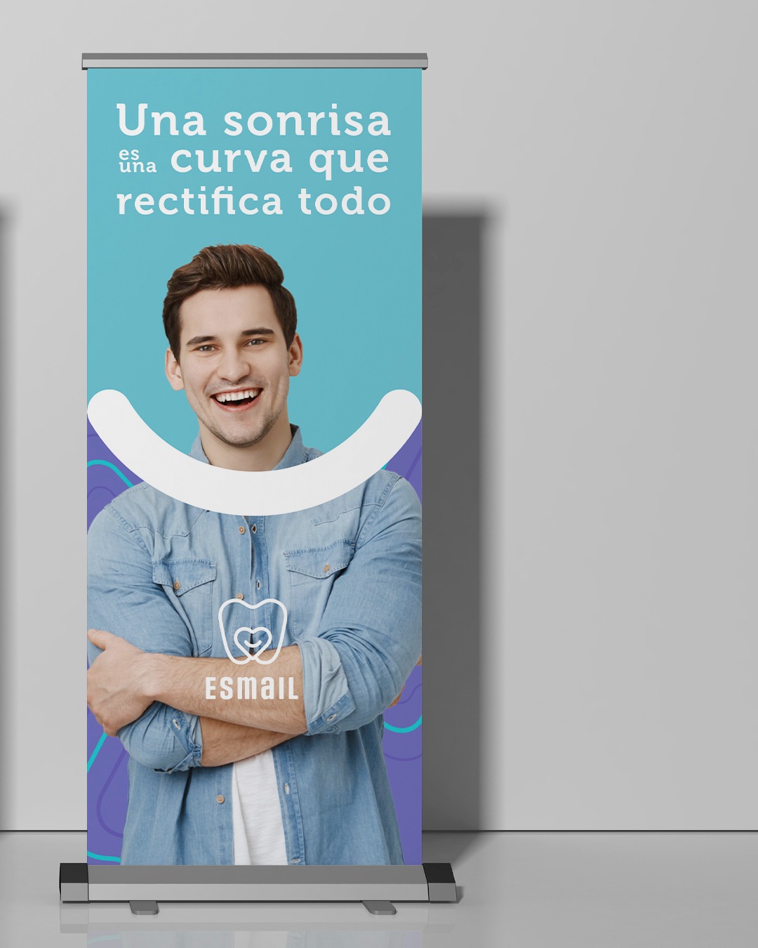 Roll-up z uśmiechniętym mężczyzną i hasłem 'Una sonrisa es una curva que rectifica todo' oraz logo 'ESMAIL' w kształcie zęba z sercem.