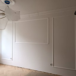 Paweł Rzeszot - Białe ściany z dekoracyjną sztukaterią w formie prostokątnych paneli, zabezpieczona lampa wisząca, parkiet w jodełkę. Wnętrze w trakcie prac wykończeniowych.