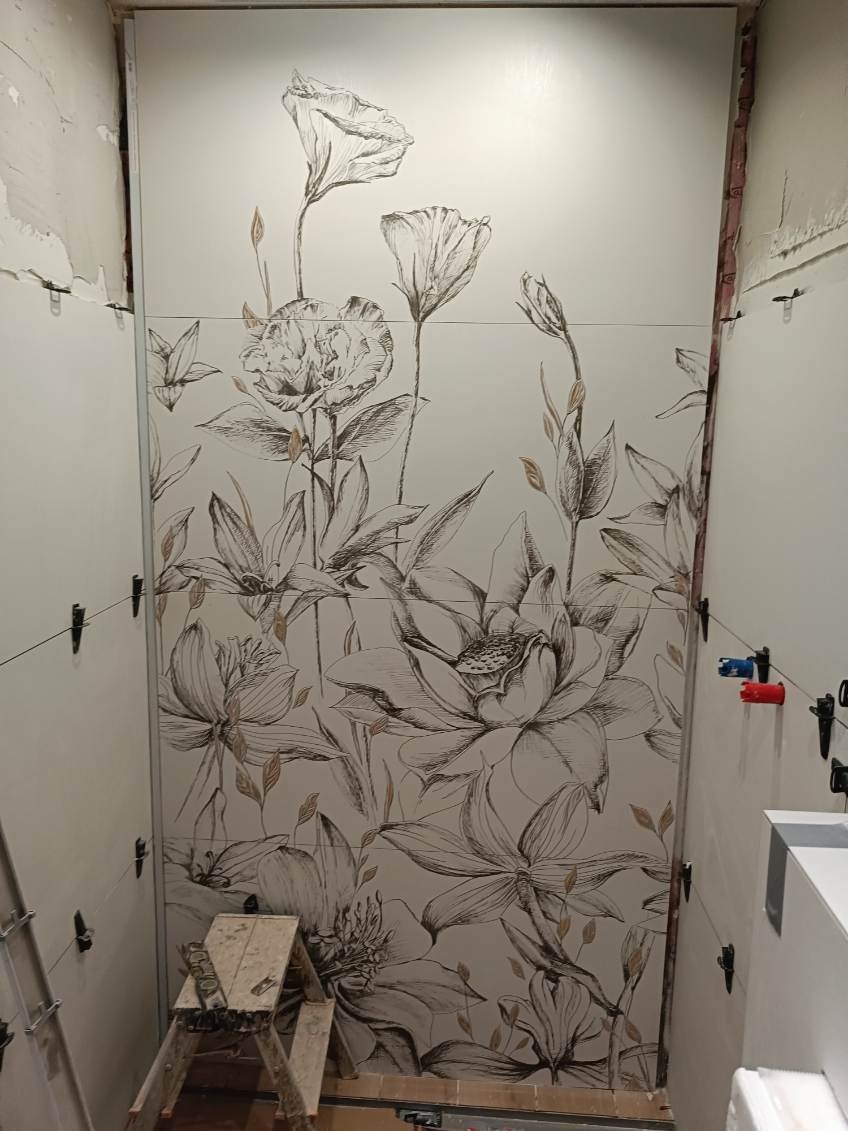 Układanie płytek z motywem kwiatowym w łazience, widoczne krzyżyki dystansowe i drabina.