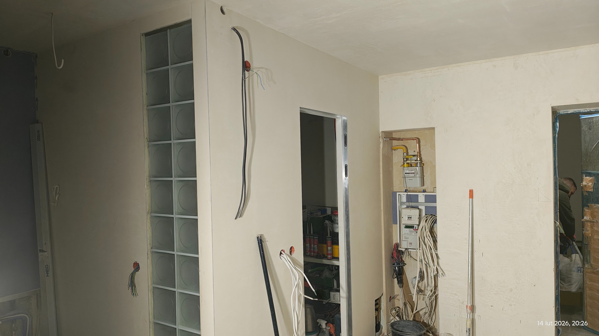 Wnętrze w trakcie tynkowania: ściany z instalacją elektryczną, widoczne bloki szklane i narzędzia. Etap prac wykończeniowych w mieszkaniu.