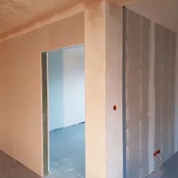 Wnętrze w trakcie remontu: ściany działowe z płyt gipsowo-kartonowych, widoczne łączenia płyt wymagające szpachlowania, surowy stan wykończenia.