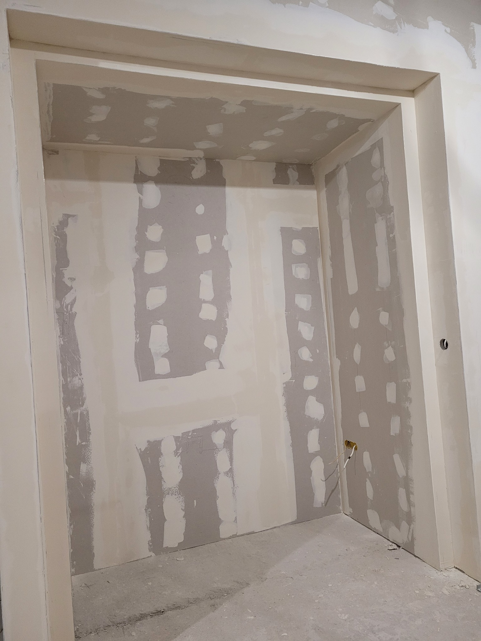 Wnęka w ścianie z widocznymi śladami po łataniu i szpachlowaniu, przygotowana do dalszych prac wykończeniowych, z wystającymi przewodami elektrycznymi.