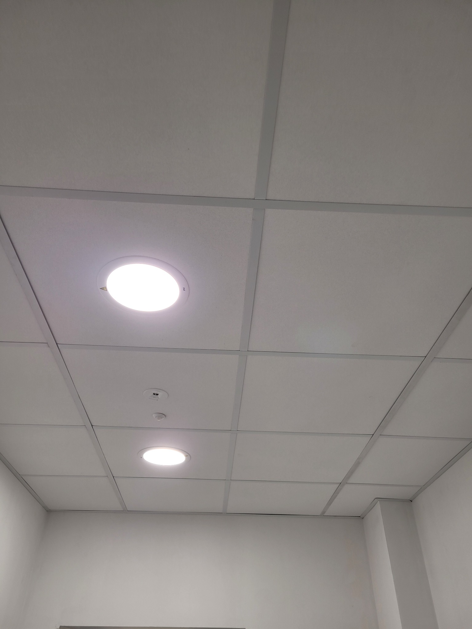 Kasetonowy sufit podwieszany z okrągłymi lampami LED wpuszczonymi w panele, widok z dołu.