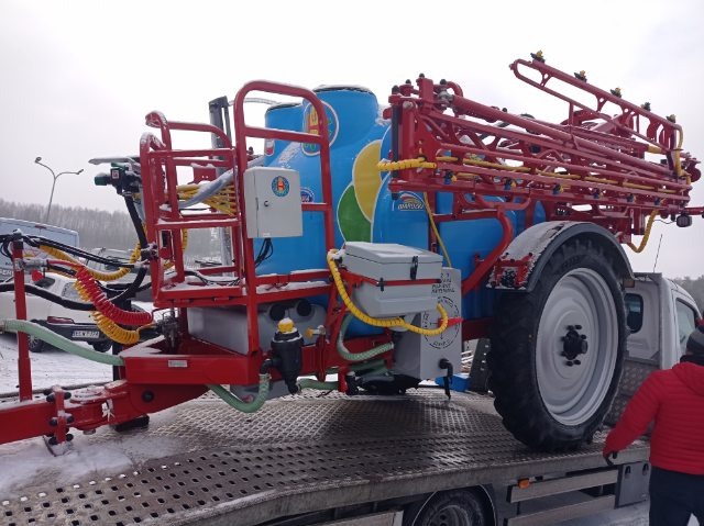 Opryskiwacz polowy, niebiesko-czerwony, z żółtymi elementami, na lawecie transportowej w Kutnie, lekko przyprószony śniegiem.