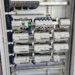 Rozdzielnica elektryczna z licznymi zabezpieczeniami, przewodami i szynami. Widoczne detale montażu i połączeń.