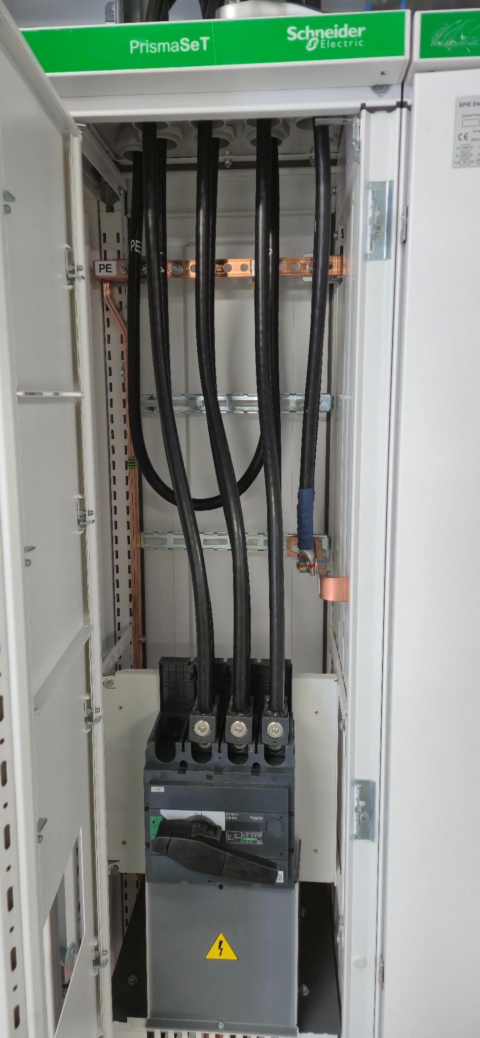 Rozdzielnica elektryczna PrismaSeT Schneider Electric z podłączonymi grubymi przewodami wewnątrz szafy. Widoczne szyny PE i elementy zabezpieczeń.