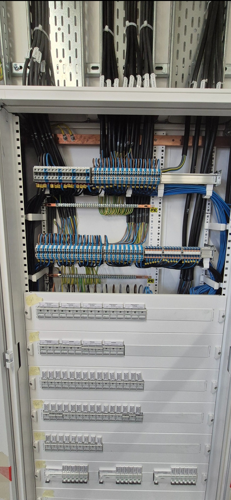 Rozdzielnia elektryczna z precyzyjnie ułożonymi kablami i bezpiecznikami. Widoczne listwy zaciskowe i oznaczenia. Estetyczne i profesjonalne wykonanie instalacji.