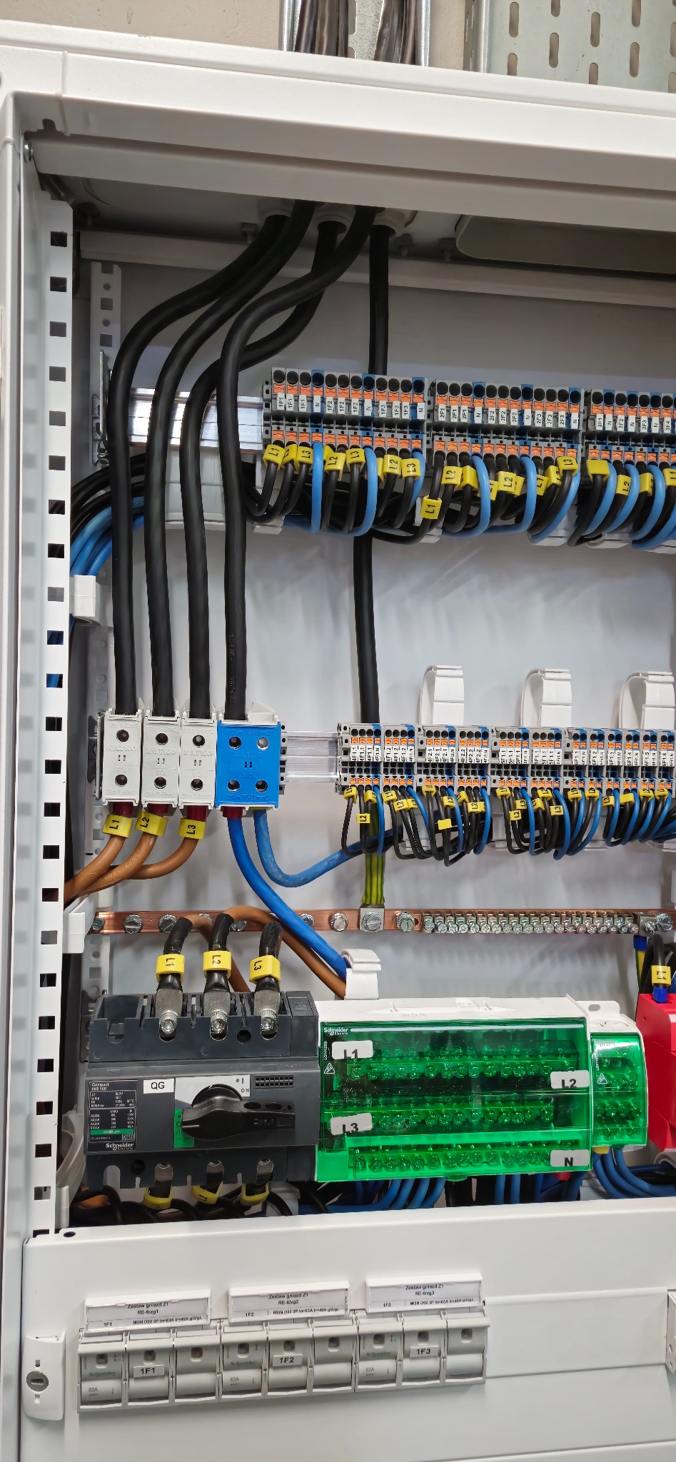 Rozdzielnica elektryczna w szafie sterowniczej, z widocznymi przewodami, bezpiecznikami i elementami łączeniowymi. Precyzyjny montaż instalacji.