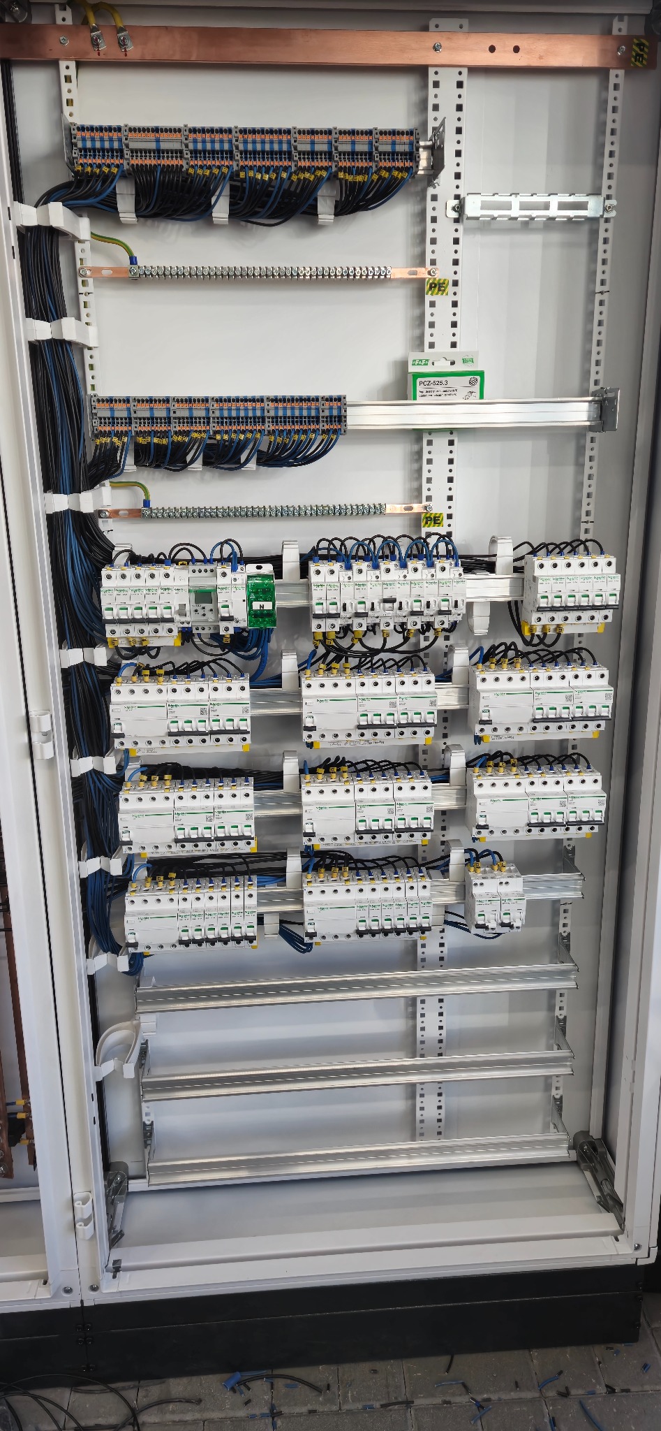 Rozdzielnica elektryczna z licznymi zabezpieczeniami, przewodami i szynami. Widoczne detale montażu i połączeń.