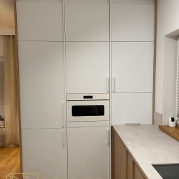 STOKŁOSA - Meble na wymiar RAFAŁ STOKŁOSA - Biała zabudowa kuchenna z piekarnikiem i blatem w odcieniach szarości, z drewnianymi akcentami. Minimalistyczny design, nowoczesne wykończenie.
