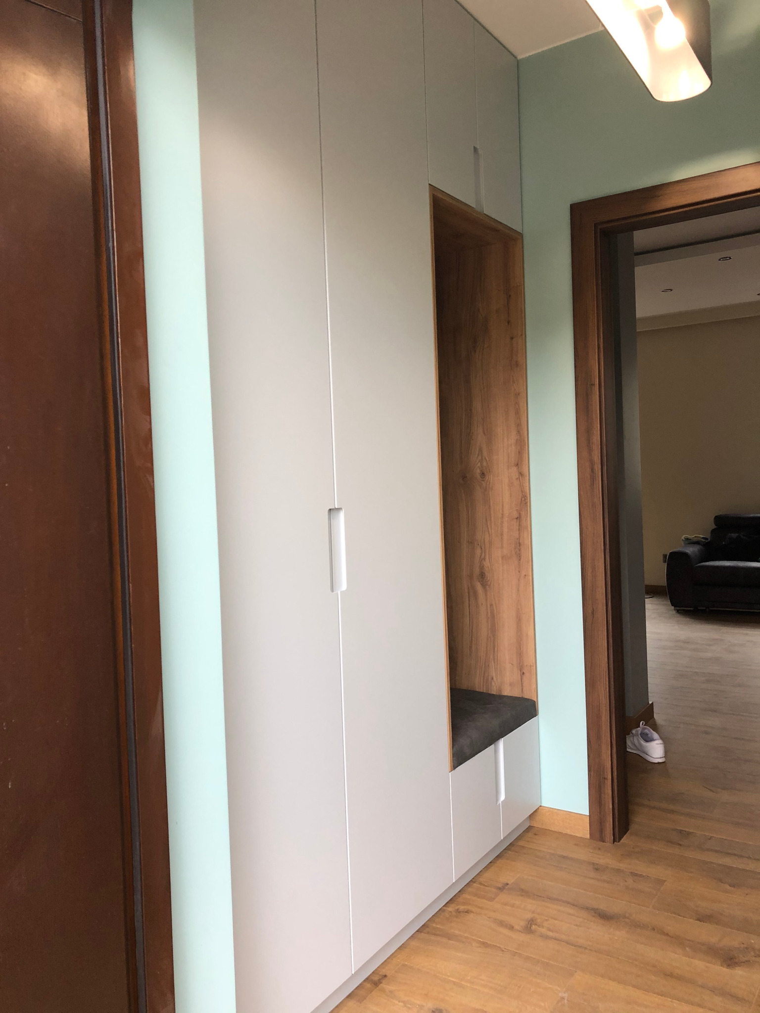 Biała szafa wnękowa z drewnianą wnęką i siedziskiem w Bulowicach, widoczna z perspektywy korytarza z drewnianą podłogą i drzwiami.