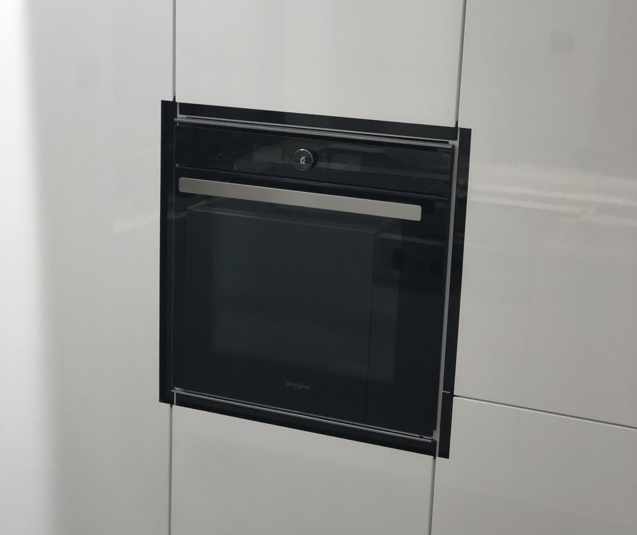 Wbudowany piekarnik marki Whirlpool z czarnym obramowaniem, umieszczony w białej, lakierowanej zabudowie kuchennej.