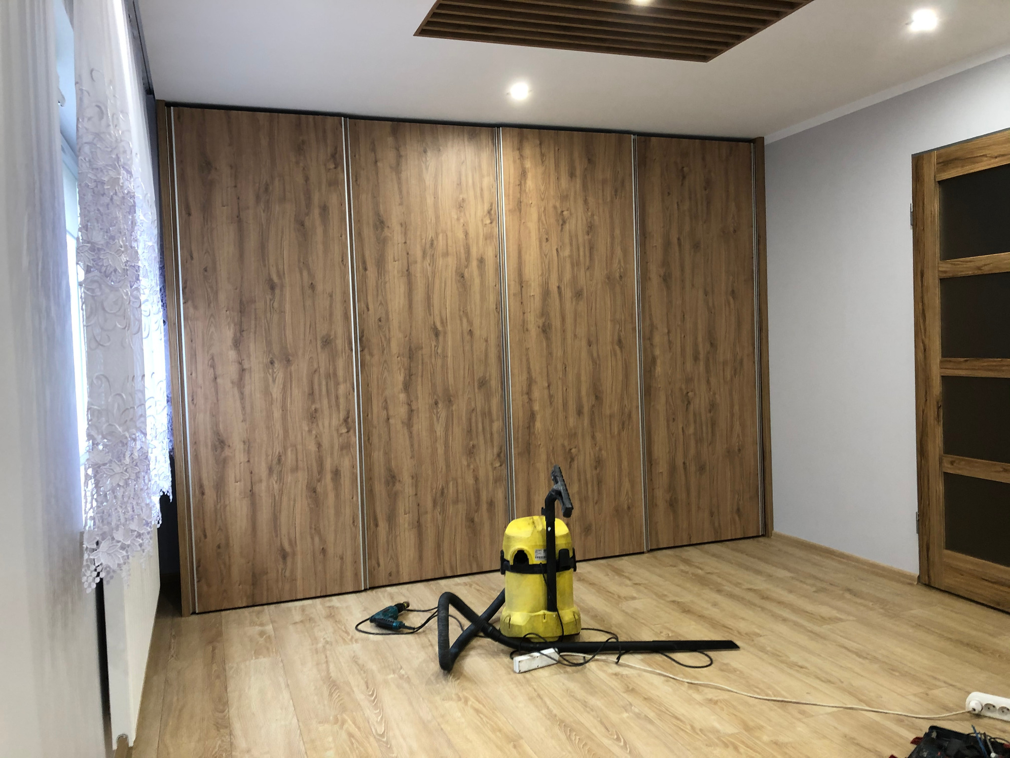 Duża szafa przesuwna z drewnopodobnymi frontami i srebrnymi wstawkami, widoczny odkurzacz i wiertarka na podłodze po montażu.