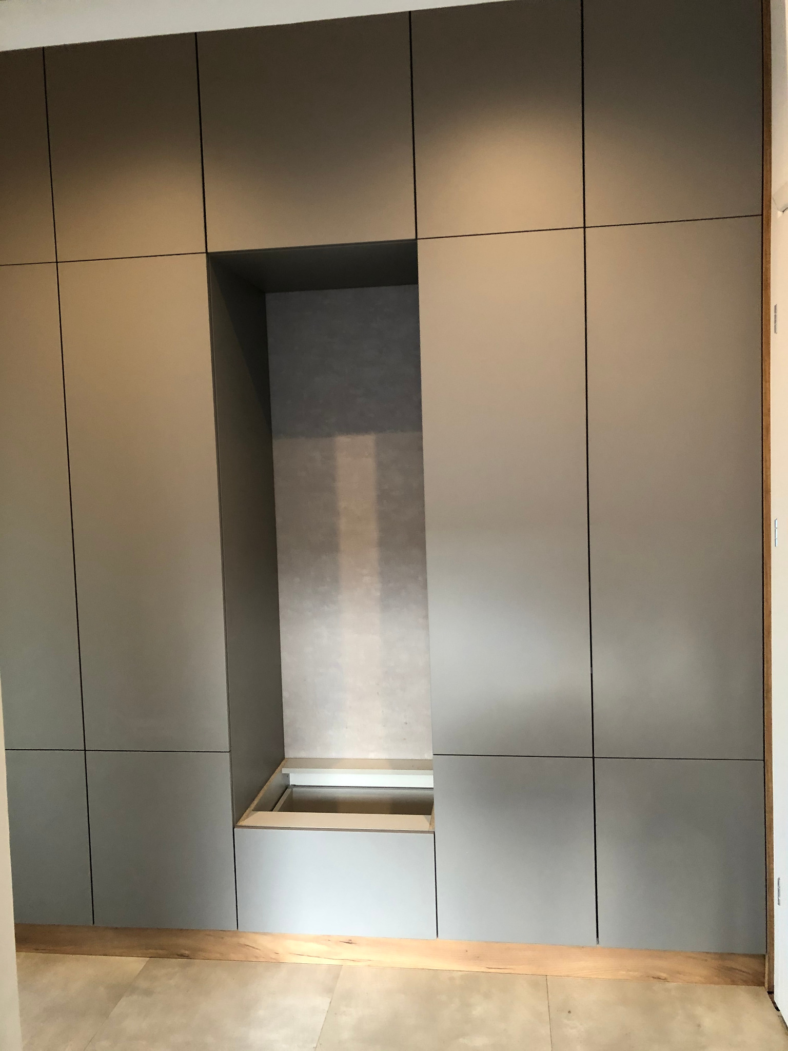 Szara zabudowa meblowa z wnęką i dolną szufladą, widok z dołu na fragment podłogi.