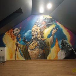 Greenwood Grzegorz Dziergas - Imponujący mural w pokoju na poddaszu przedstawiający szamana w nakryciu głowy z piór, czaszkę zwierzęcą i wyjącego wilka na tle kosmosu i tęczy, z klimatyzacją i drewnianą podłogą w dolnej części.