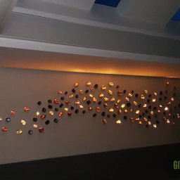 Greenwood Grzegorz Dziergas - Ściana z dekoracyjnym oświetleniem punktowym w kształcie nieregularnych bryłek, podświetlona listwa LED pod sufitem, widoczne logo firmy w rogu.