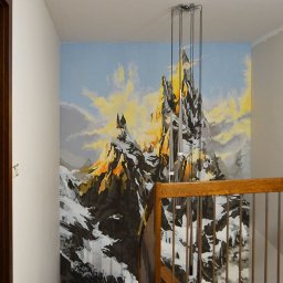 Greenwood Grzegorz Dziergas - Malowidło górskiego krajobrazu z zamkiem na ścianie klatki schodowej w Opolu, widoczne zza drewnianej balustrady schodów.