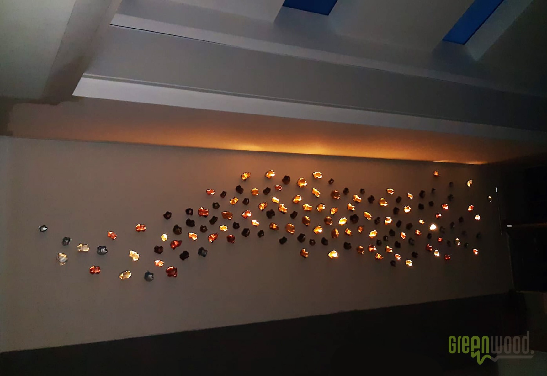 Ściana z dekoracyjnym oświetleniem punktowym w kształcie nieregularnych bryłek, podświetlona listwa LED pod sufitem, widoczne logo firmy w rogu.