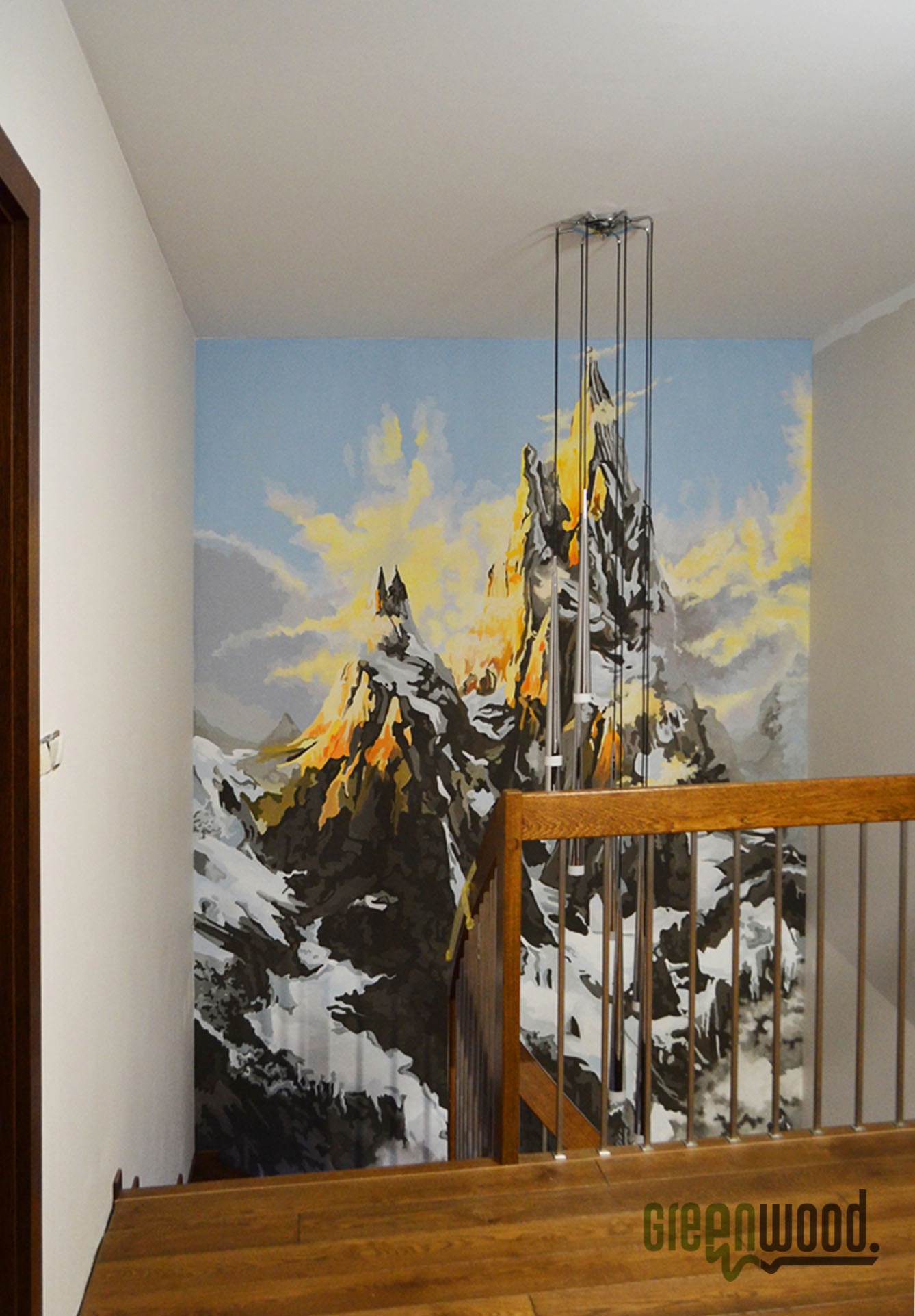 Malowidło górskiego krajobrazu z zamkiem na ścianie klatki schodowej w Opolu, widoczne zza drewnianej balustrady schodów.