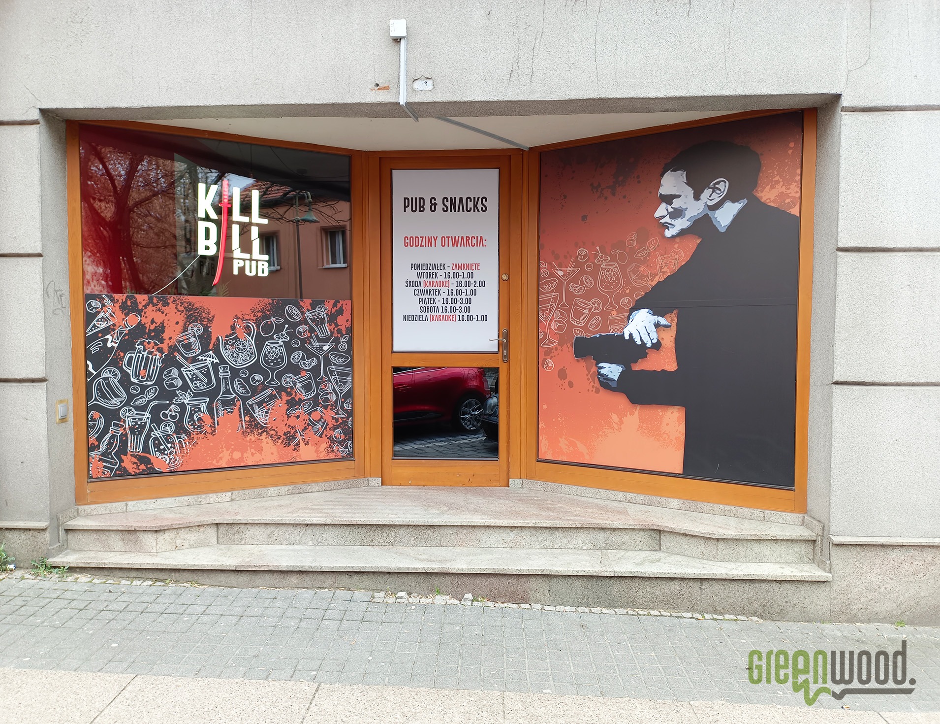 Fasada pubu z grafikami nawiązującymi do filmu Kill Bill na oknach i drzwiach, widoczne godziny otwarcia i logo Greenwood.