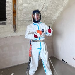 Delta Pur Izolacje - Pracownik w kombinezonie po ociepleniu poddasza pianką PUR w Nadmie, z pistoletem natryskowym i kciukiem w górę. Ściany pokryte pianą.