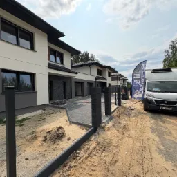 Nowoczesne domy w zabudowie szeregowej z szarą elewacją i czarną stolarką okienną. Na pierwszym planie utwardzona kostką ścieżka i firmowy van Delta Pur.