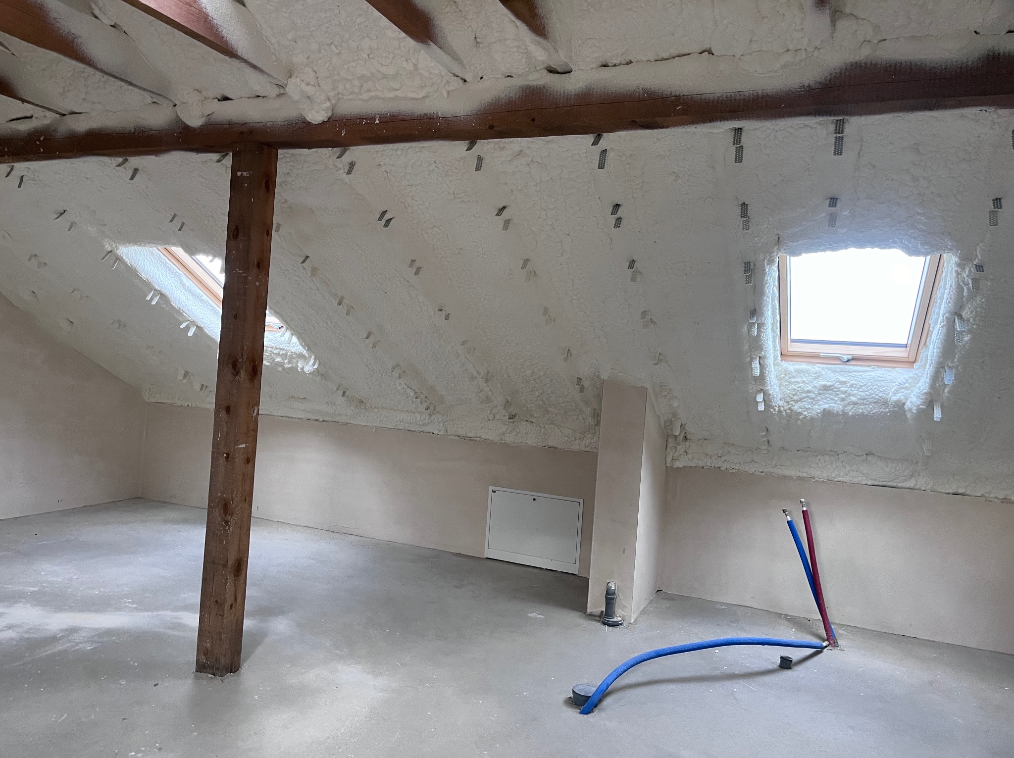 Poddasze po ociepleniu pianką PUR, widoczne okna dachowe i drewniany słup podtrzymujący konstrukcję dachu. Instalacja wodna na posadzce.