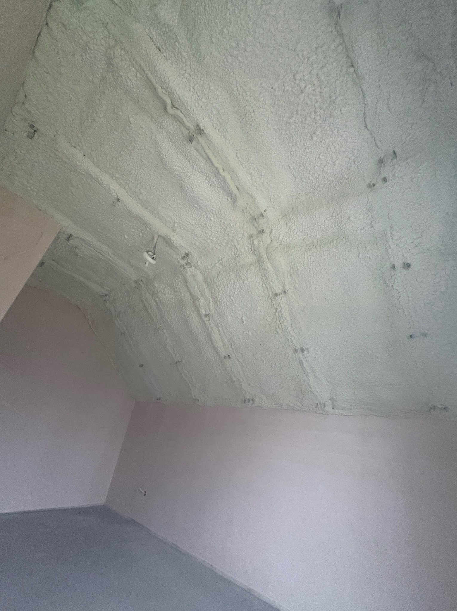 Poddasze po ociepleniu pianką PUR, widoczne równomierne pokrycie izolacją. Elementy konstrukcyjne zakryte pianą, ściany w jasnym kolorze, surowa podłoga.