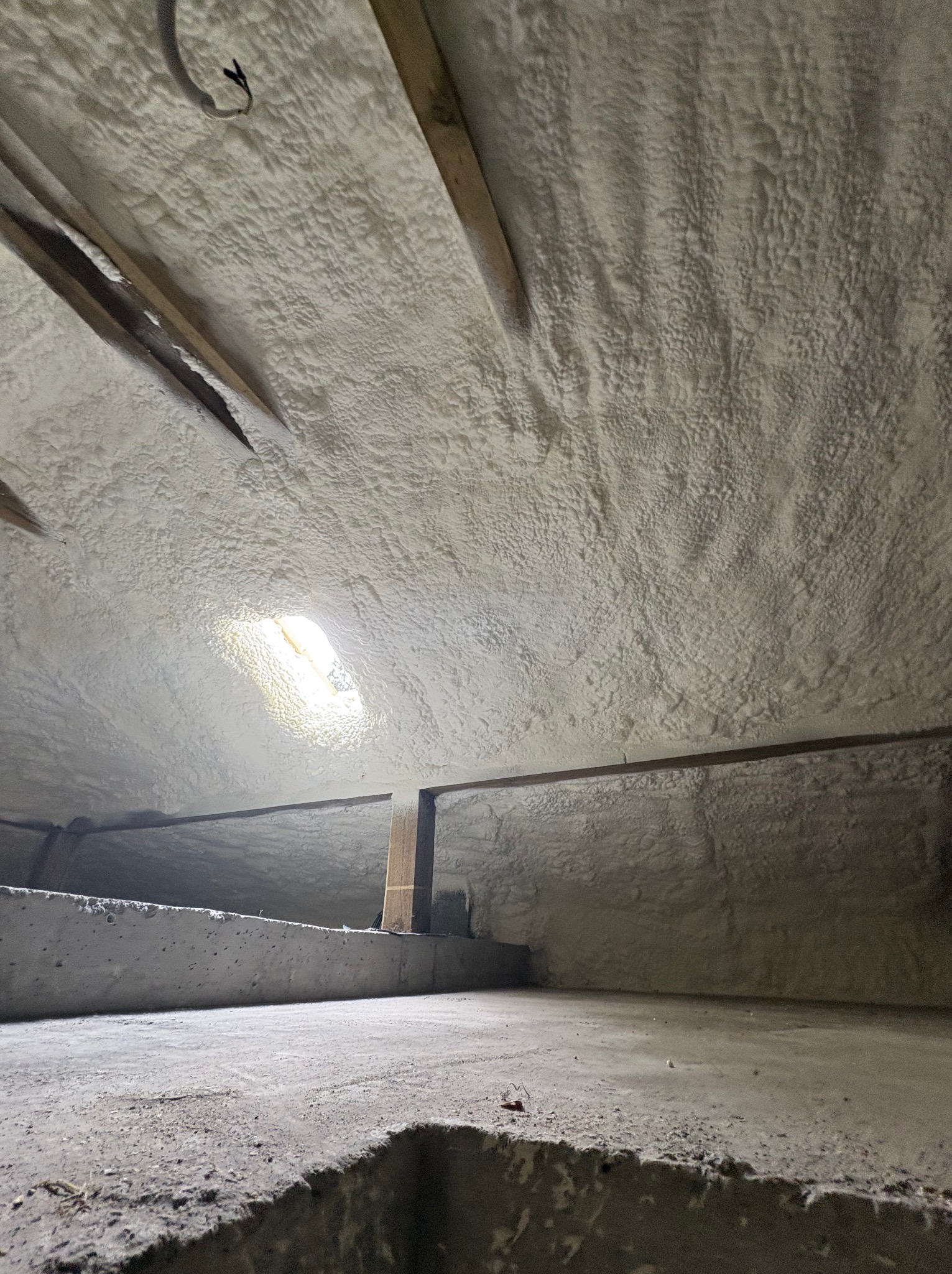 Poddasze ocieplone pianką PUR, widoczne drewniane elementy konstrukcyjne i betonowa podstawa. Oświetlenie wpada przez okno dachowe.