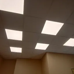 Kwadratowe panele sufitowe z wbudowanym oświetleniem LED w pomieszczeniu z beżowymi ścianami, widok z dołu pod kątem.