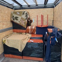 Kacper Kacper - Meble zabezpieczone folią i kocami w przestrzeni ładunkowej busa. Widoczne krzesła i elementy garderoby. Transportowany dobytek przygotowany do przewozu.