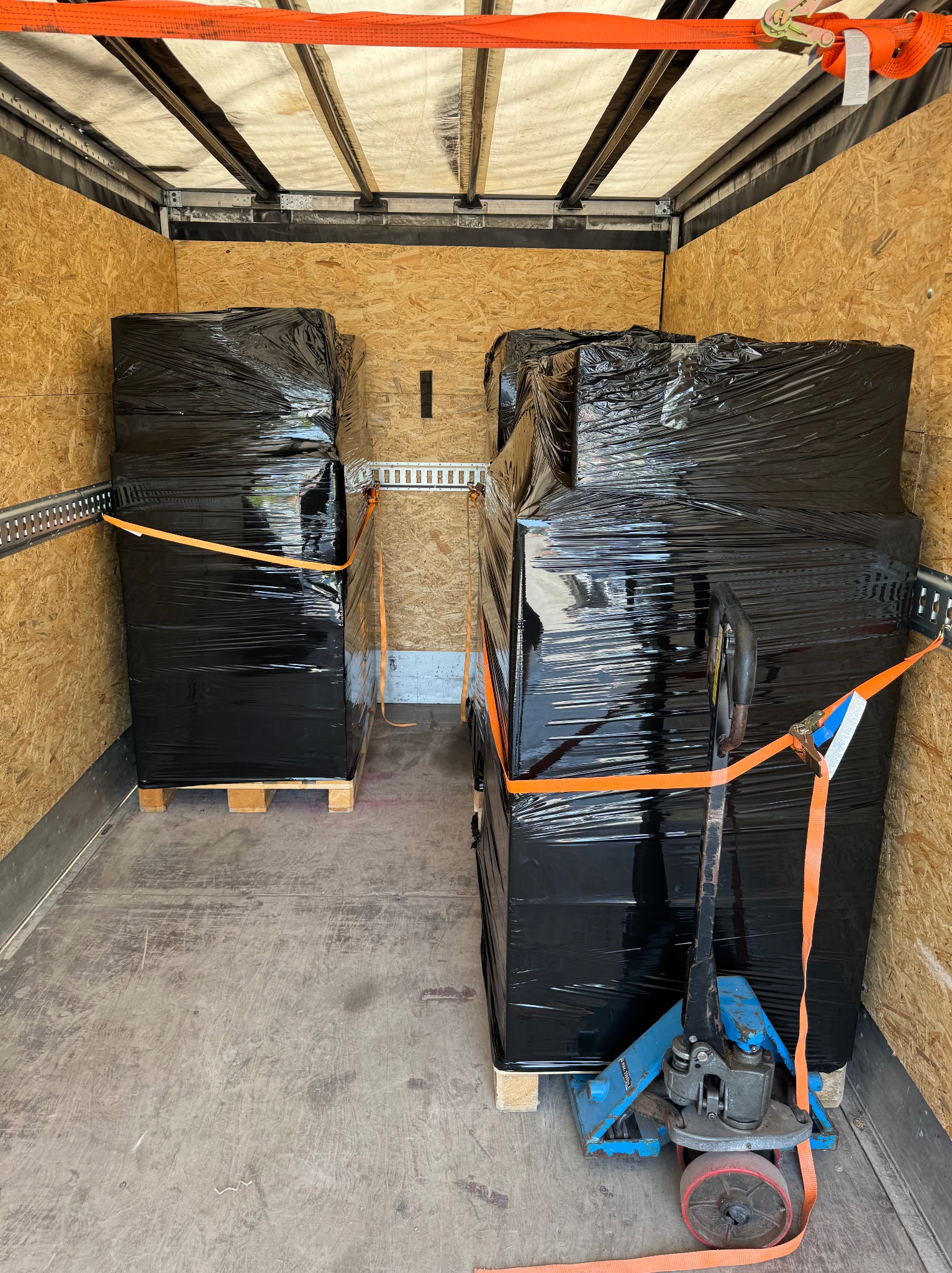 Załadunek towaru na paletach w busie zabezpieczonego pasami transportowymi, Łask. W tle widoczna ściana pojazdu z płyty OSB.