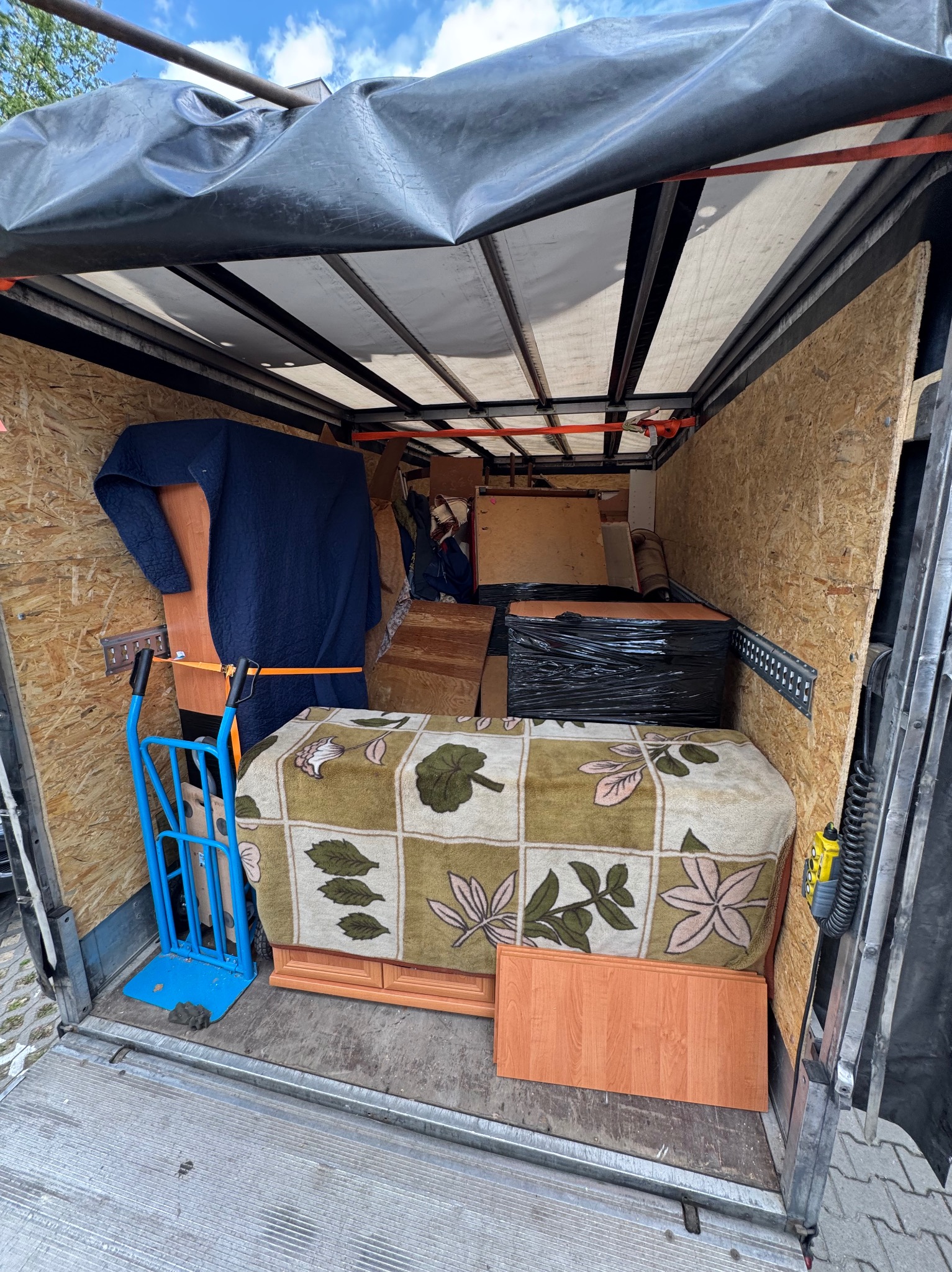 Wnętrze przestrzeni ładunkowej busa wypełnione meblami i przedmiotami, zabezpieczonymi do transportu podczas przeprowadzki. Widoczny wózek transportowy.