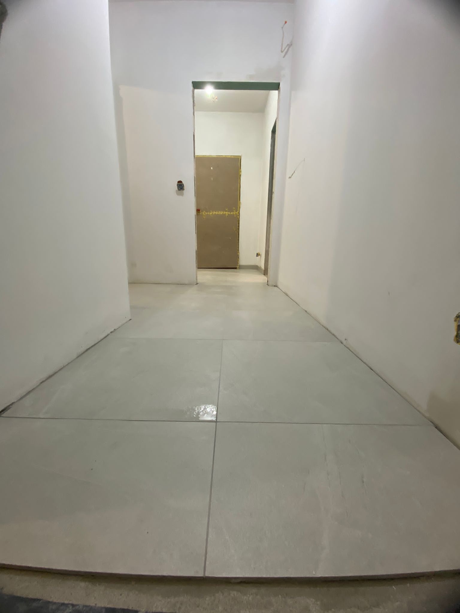 Wnętrze w trakcie prac wykończeniowych w Kórniku: widok na świeżo położone, jasnoszare płytki podłogowe w korytarzu, z widocznymi śladami po fugowaniu, oraz przygotowane do malowania ściany.