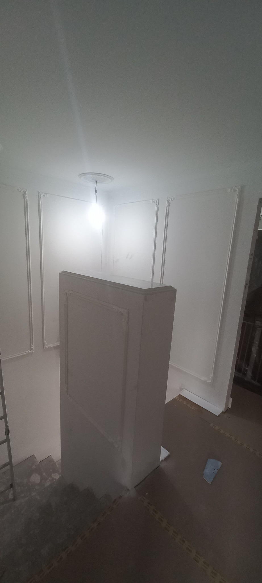 Klatka schodowa po remoncie z ozdobnymi listwami ściennymi i dekoracyjnym obramowaniem schodów, widoczna drabina i zabezpieczona podłoga.