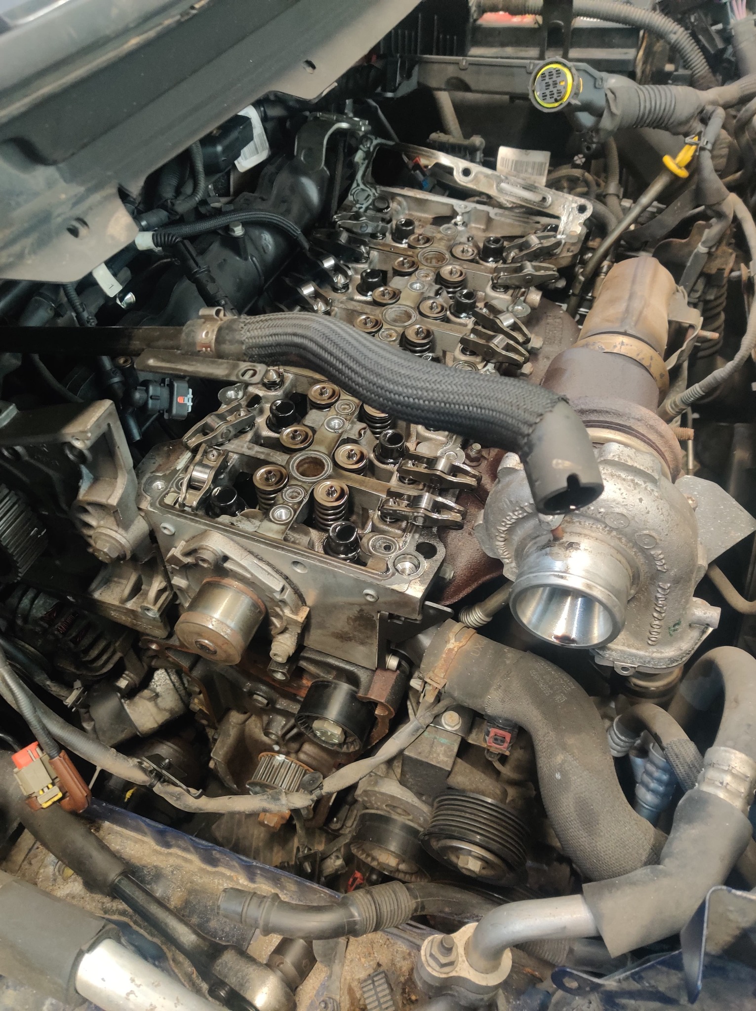 Otwarta głowica silnika z widocznymi wałkami rozrządu, sprężynami zaworowymi i turbosprężarką, w trakcie naprawy lub przeglądu, z widocznymi przewodami i elementami osprzętu.