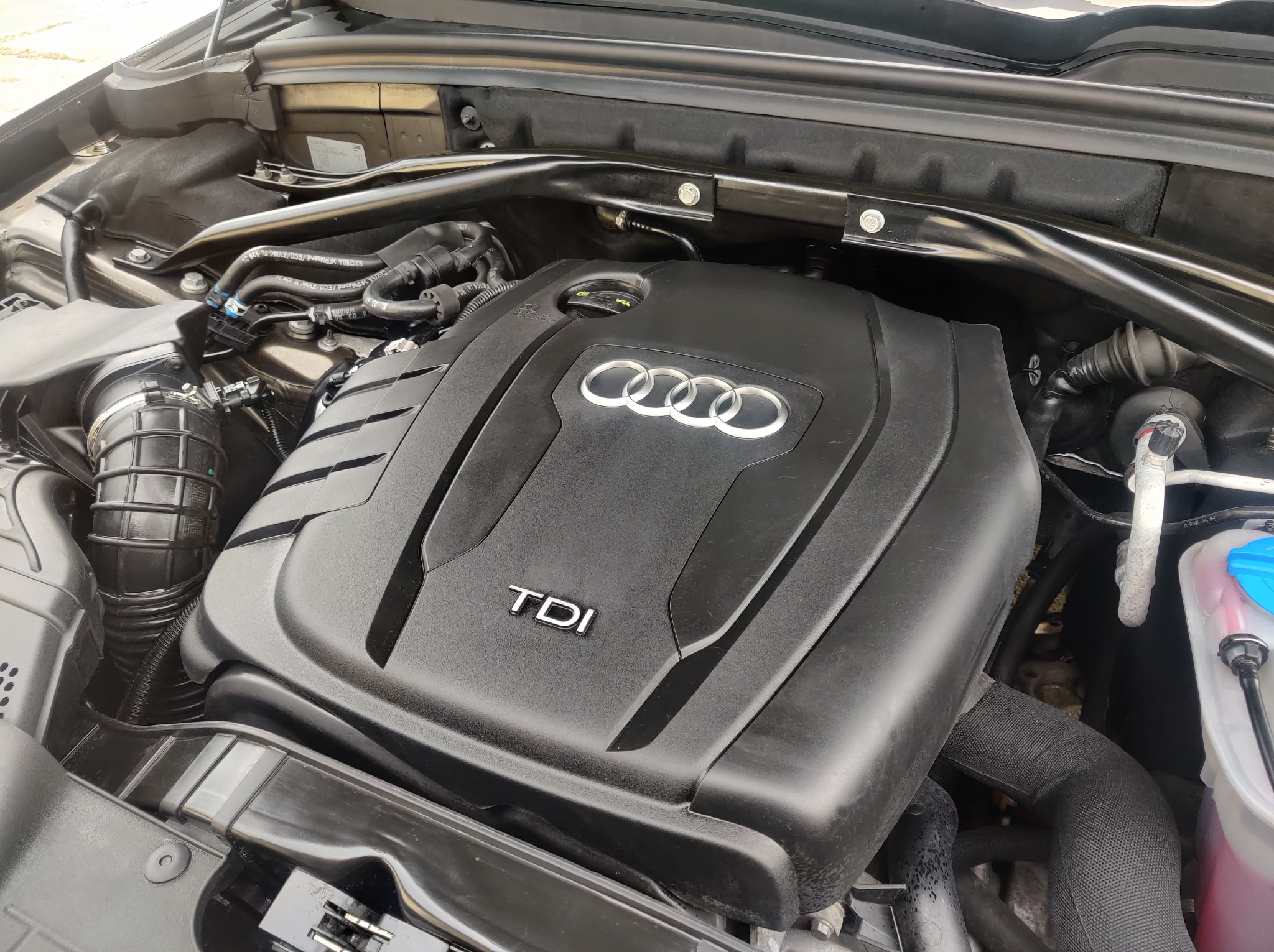Widok z góry na otwartą maskę samochodu Audi, eksponujący silnik TDI z widocznym logo producenta i elementami układu chłodzenia.