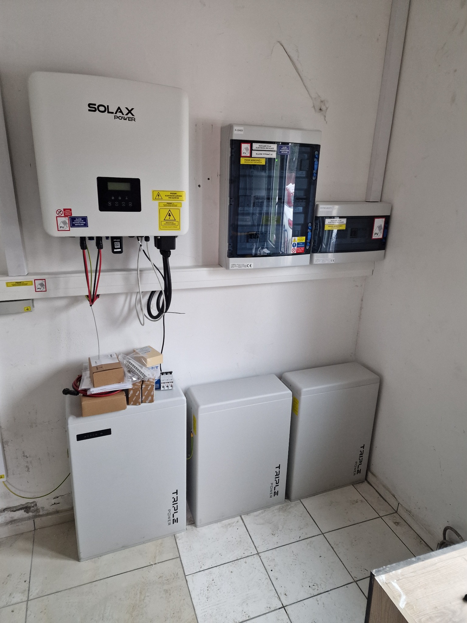 Instalacja wewnętrzna: Inwerter Solax Power podłączony do rozdzielnicy elektrycznej i trzech akumulatorów Triple Power. Widoczne okablowanie i elementy montażowe.