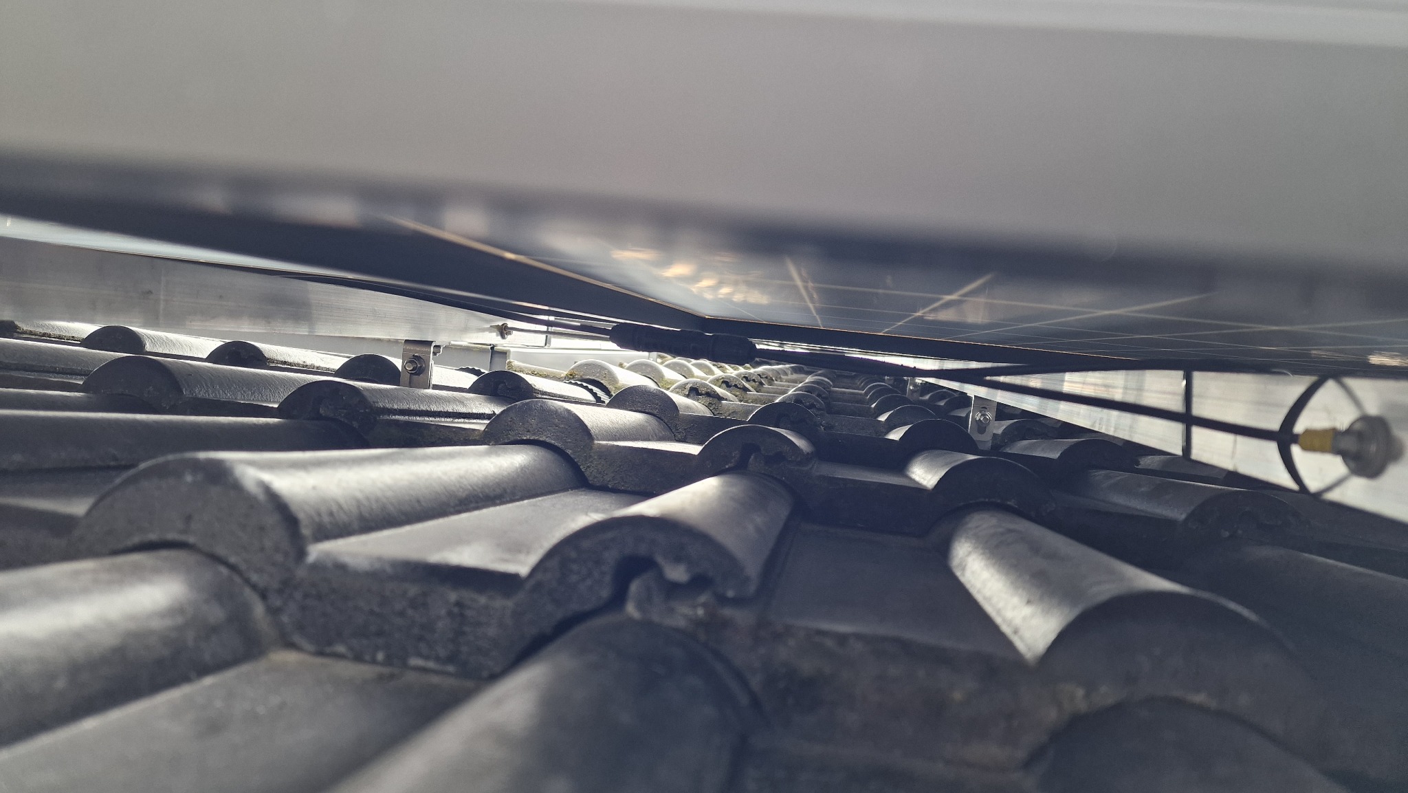 Montaż paneli słonecznych na dachu pokrytym ceramiczną dachówką, widok z dołu ukazujący konstrukcję mocującą panele.