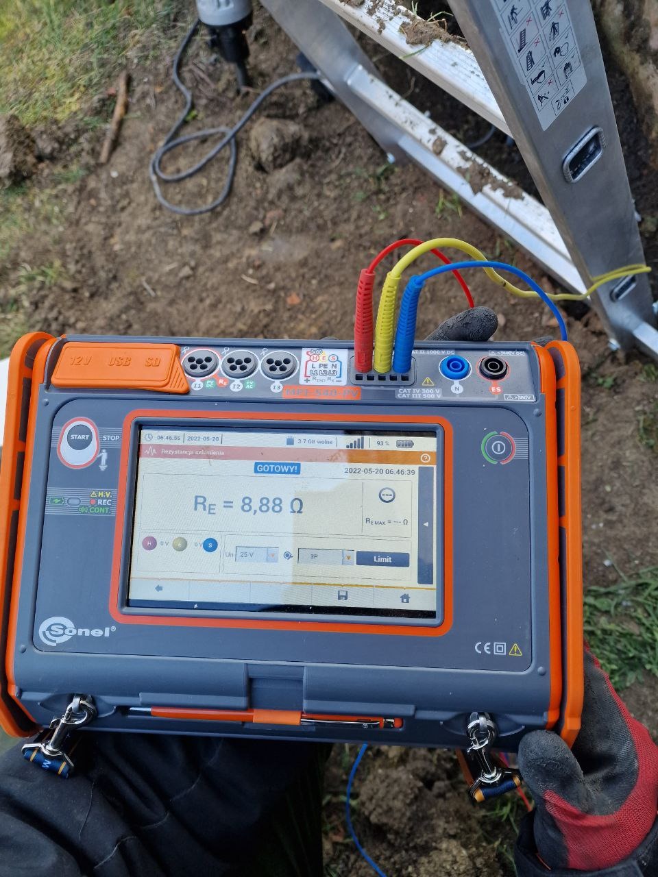 Miernik Sonel z podłączonymi przewodami pomiarowymi, wyświetlający wynik rezystancji uziemienia 8,88 Ω, ustawiony na ziemi obok drabiny podczas pomiarów.