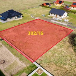 Tomasz Winnicki - Działka budowlana oznaczona czerwoną obwódką i numerem 302/16, widok z drona na okoliczne domy i ogrody.