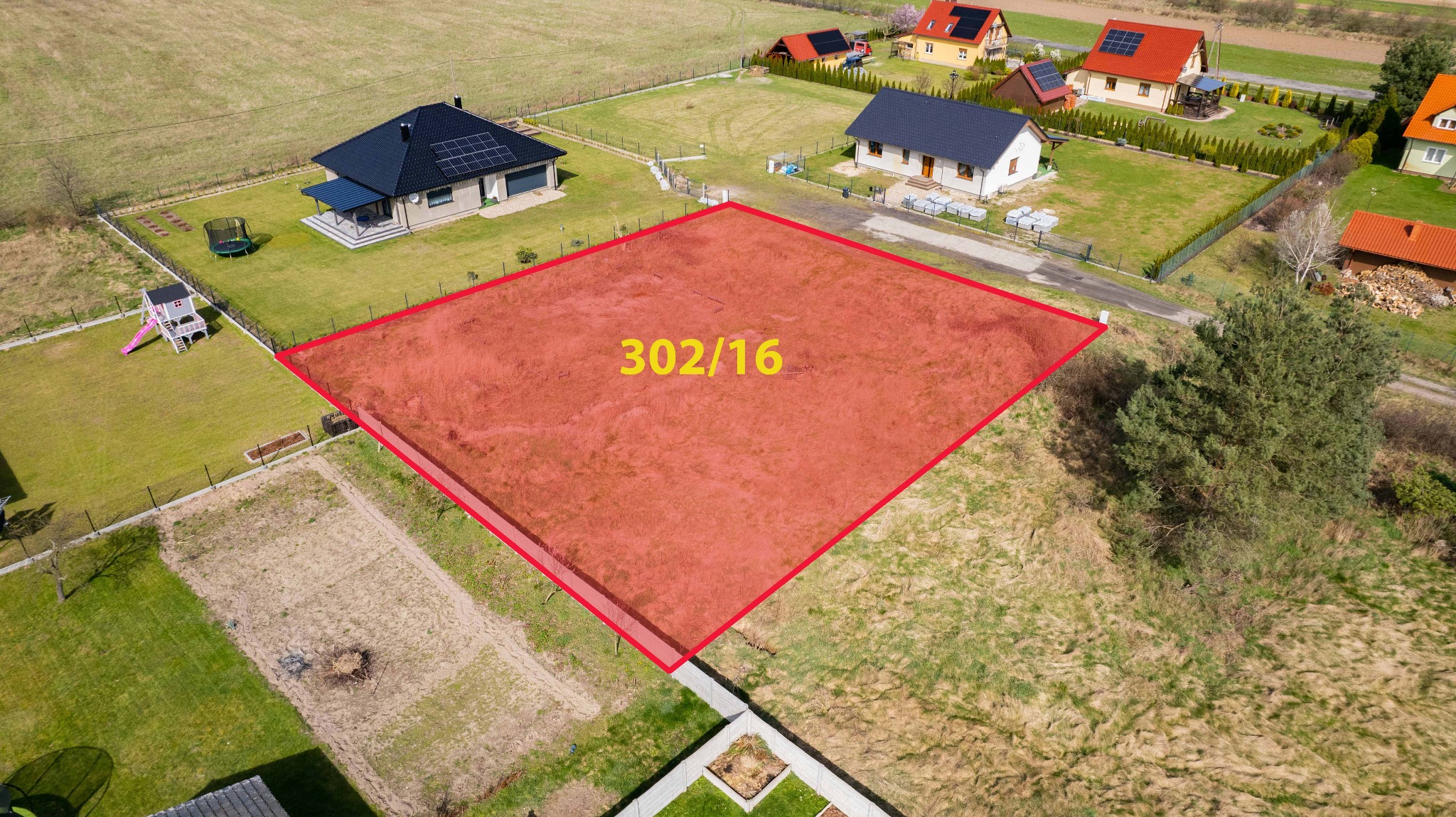 Działka budowlana oznaczona czerwoną obwódką i numerem 302/16, widok z drona na okoliczne domy i ogrody.