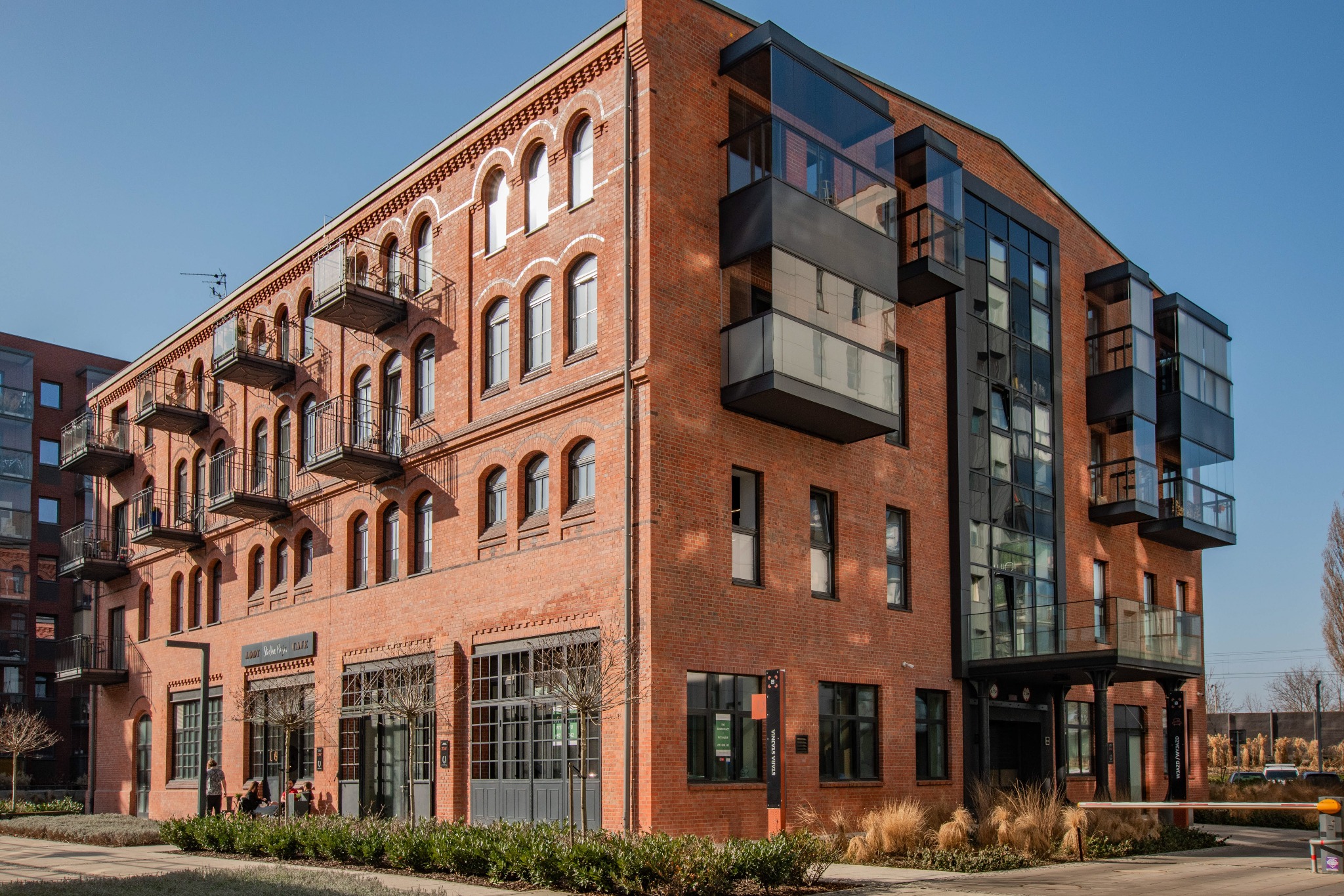 Odrestaurowany budynek z czerwonej cegły z balkonami i nowoczesnymi przeszklonymi dobudówkami, widok z zewnątrz w słoneczny dzień.