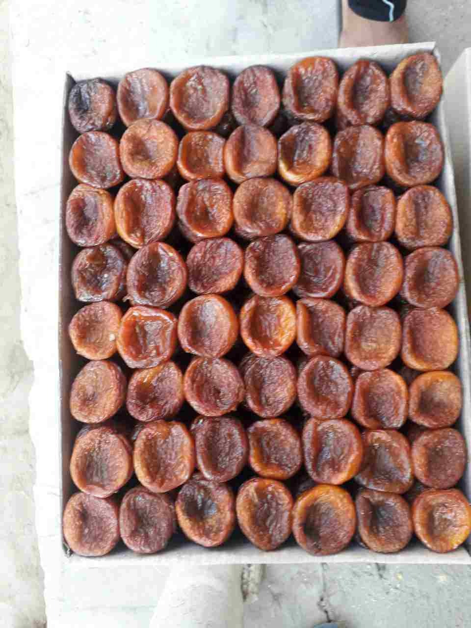 Kartonowe pudełko wypełnione suszonymi morelami ułożonymi w rzędach, widoczne nierównomierne zabarwienie owoców.