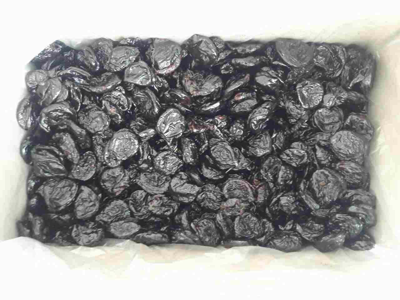 Karton wypełniony suszonymi śliwkami o ciemnej, błyszczącej powierzchni, ułożonymi ciasno obok siebie.