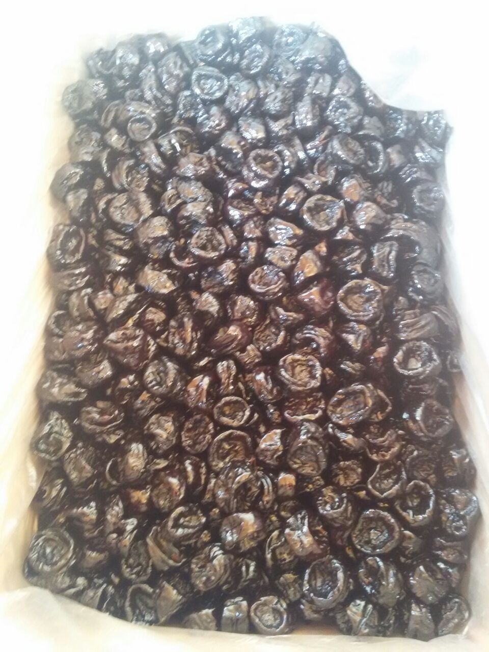 Suszone śliwki w dużym pojemniku, widoczne błyszczące powierzchnie owoców i nierównomierne oświetlenie.